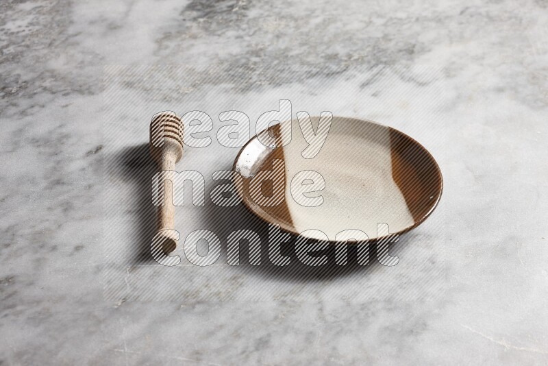 Multicolored pottery plate with wooden honey dipper on the side on grey marble background