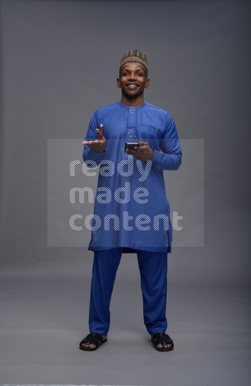 Man wearing Nigerian outfit standing texting on phone on gray background