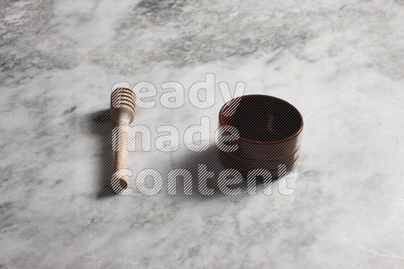 Brown pottery bowl with wooden honey dipper on the side on grey marble background