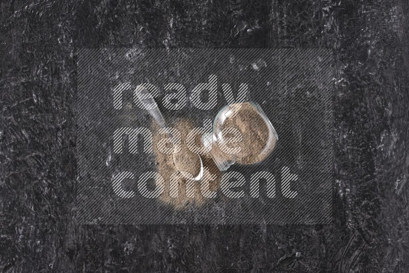 بودرة الفلفل الأسود في وعاء زجاجي مقلوب مع ملعقة معدنية مليئة بالبودرة علي خلفية سوداء