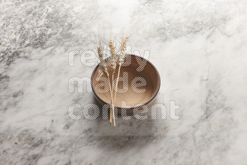 Wheat stalks on beige pottery oven bowl on grey marble background