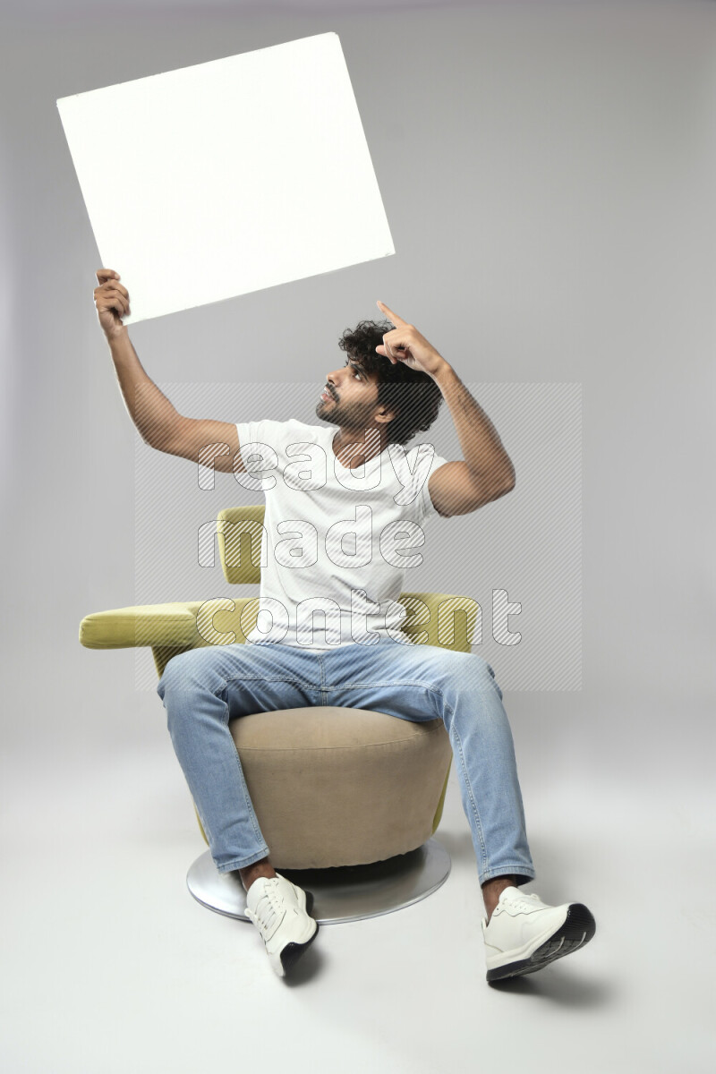 A man wearing casual sitting on a chair holding a white board on white background