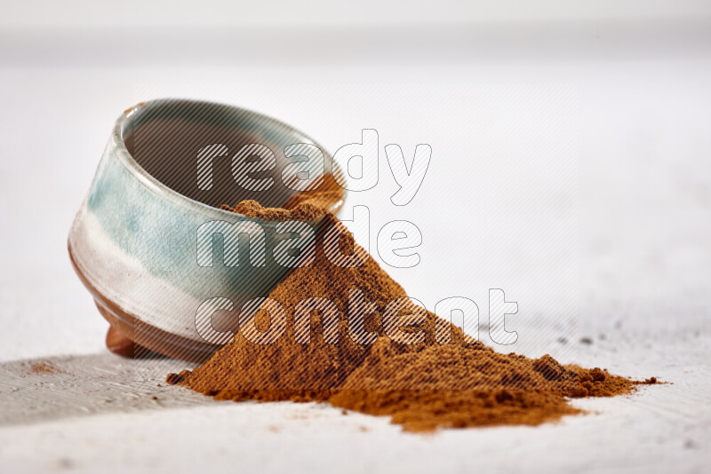 A colored pottery bowl full of ground paprika powder with fallen powder from it on white background