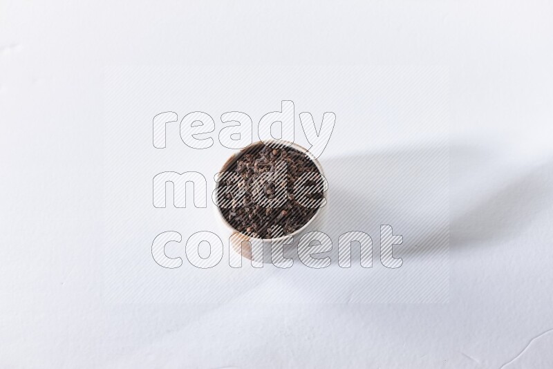 A beige ceramic bowl full of cloves on a white flooring