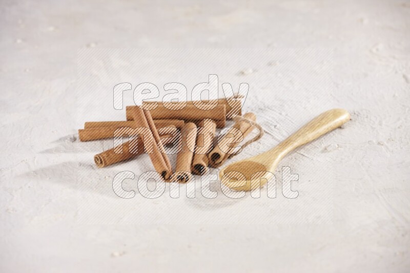 Cinnamon sticks stacked beside a wooden spoon full of cinnamon powder on white background