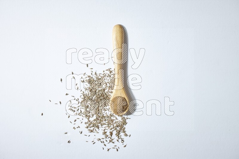 A wooden spoon full of cumin powder and cumin seeds beside it on white flooring