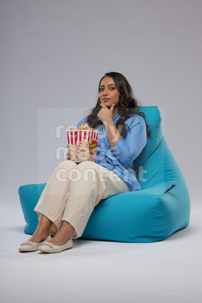 A woman sitting on a blue beanbag and eating popcorn