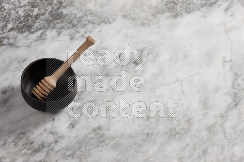 Black pottery bowl with wooden honey dipper in it on grey marble background