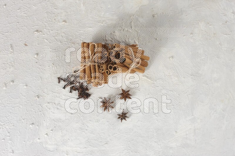 Two bounded stacks of cinnamon sticks with cloves and star anise on white background