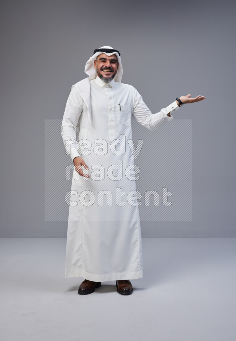 Saudi man Wearing Thob and white Shomag standing interacting with the camera on Gray background