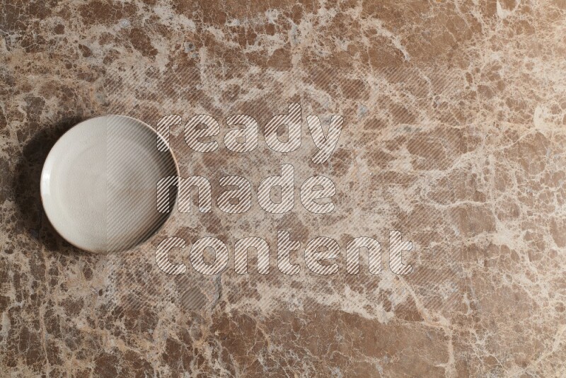 A beige pottery plate on beige marble background
