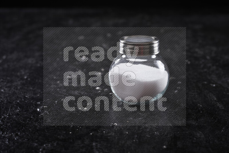 A glass jar full of fine table salt on black background