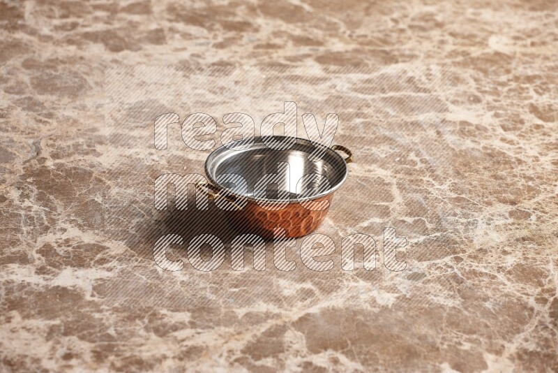 A small copper pot on beige marble background