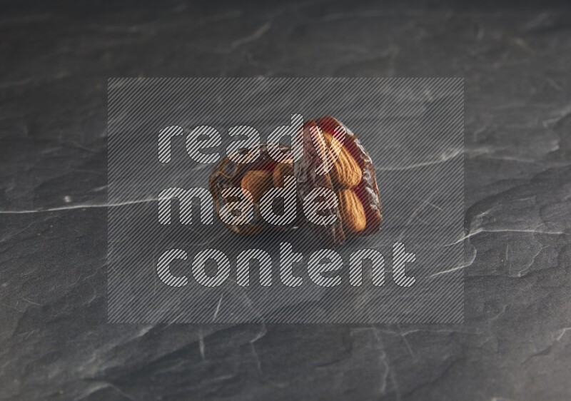 two almond stuffed madjoul dates on a black textured background