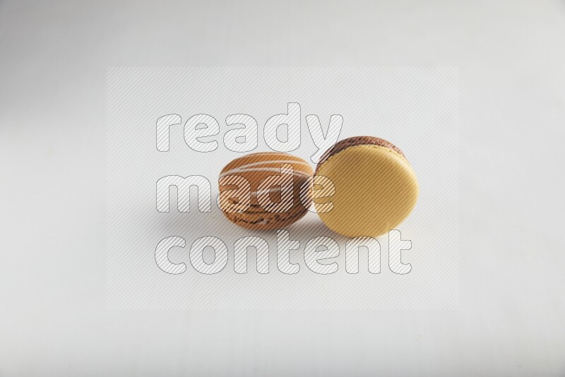 45º Shot of of two assorted Brown Irish Cream, and Yellow, and Brown Chai Latte macarons on white background