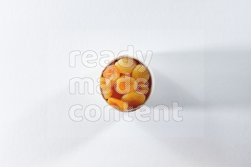 A beige ceramic bowl full of dried apricots on a white background in different angles