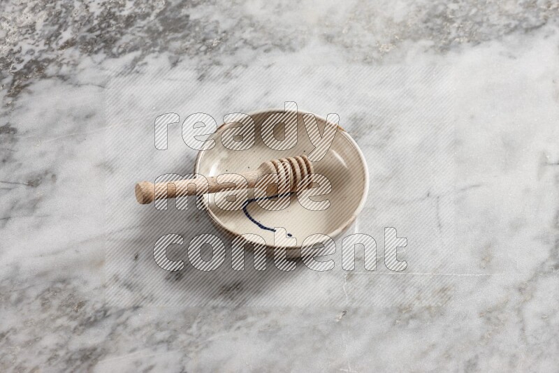 Multicolored pottery bowl with wooden honey dipper in it on grey marble background