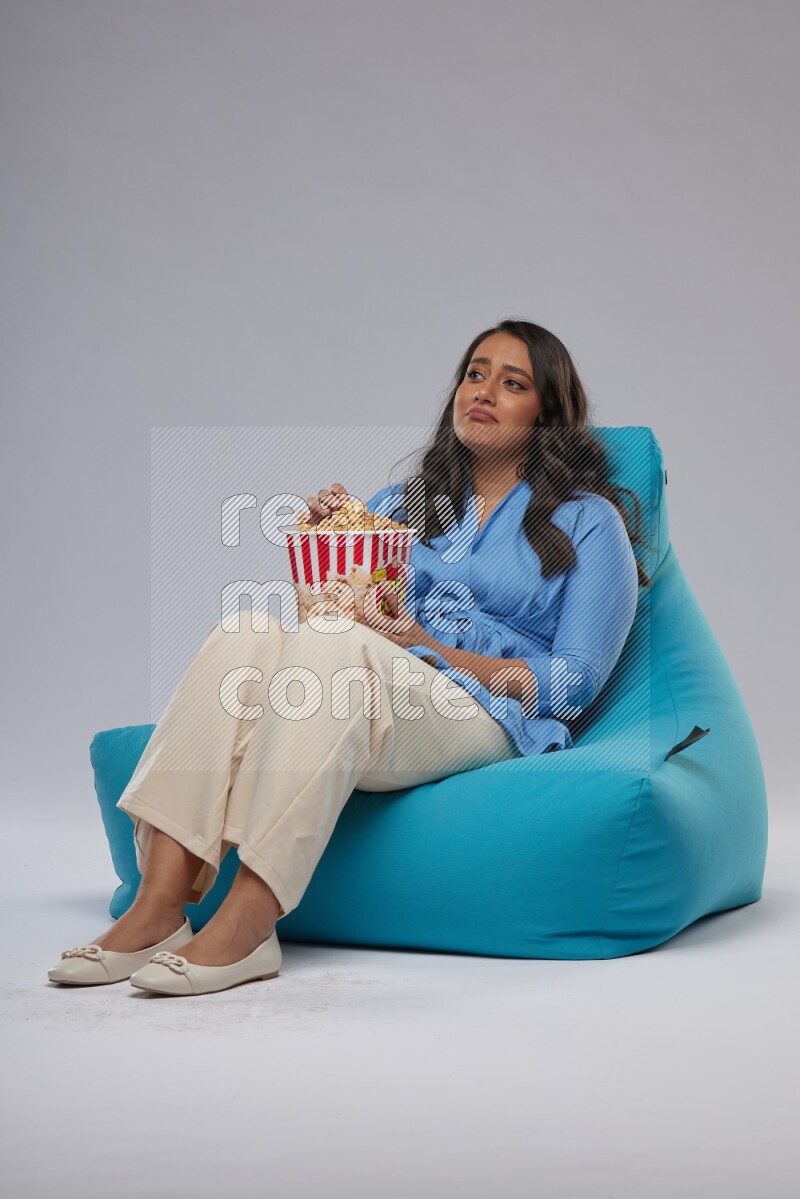 A woman sitting on a blue beanbag and eating popcorn