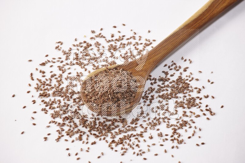 A wooden ladle full of flax seeds on a white flooring
