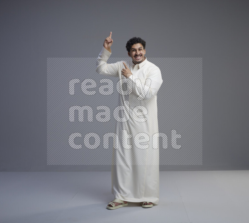 A Saudi man standing wearing thob interacting with the camera on gray background