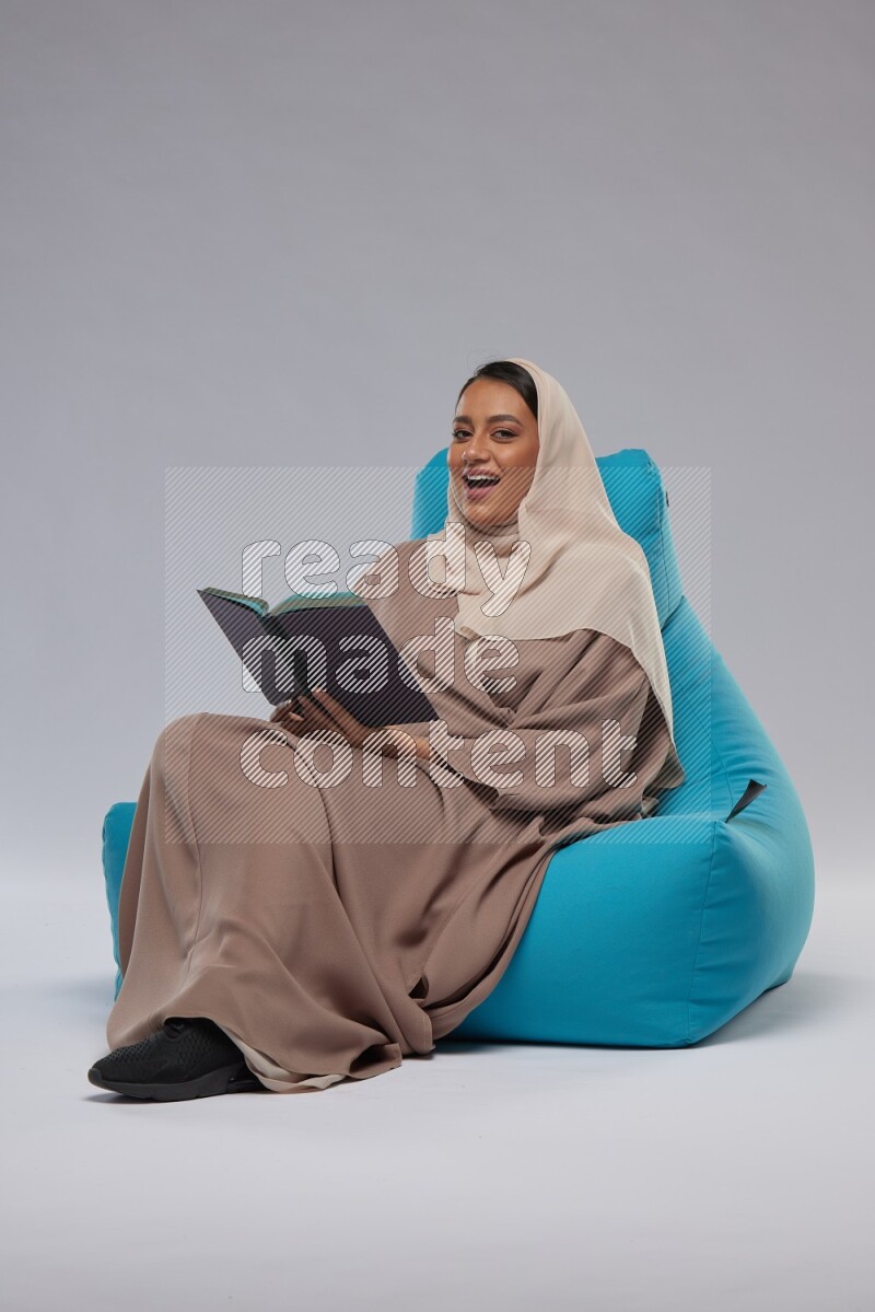 A woman sitting on a blue beanbag and reading a book