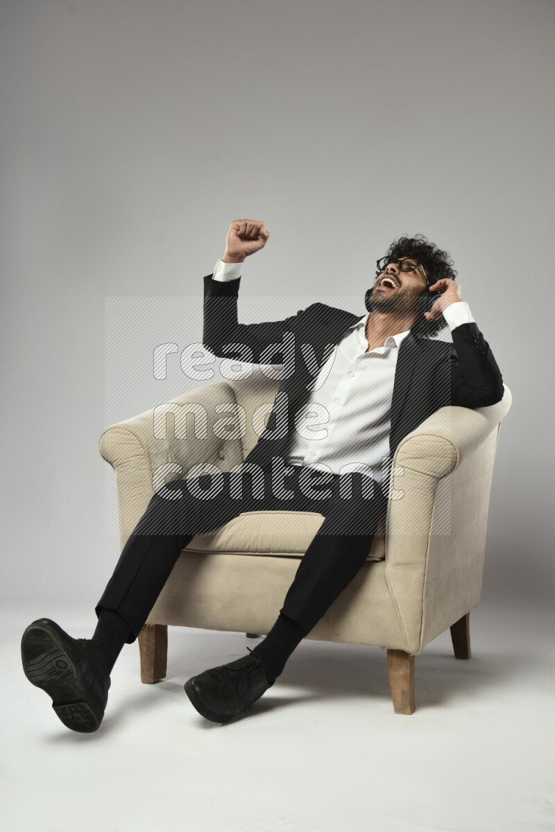 A man wearing formal sitting on a chair putting on headphones on white background