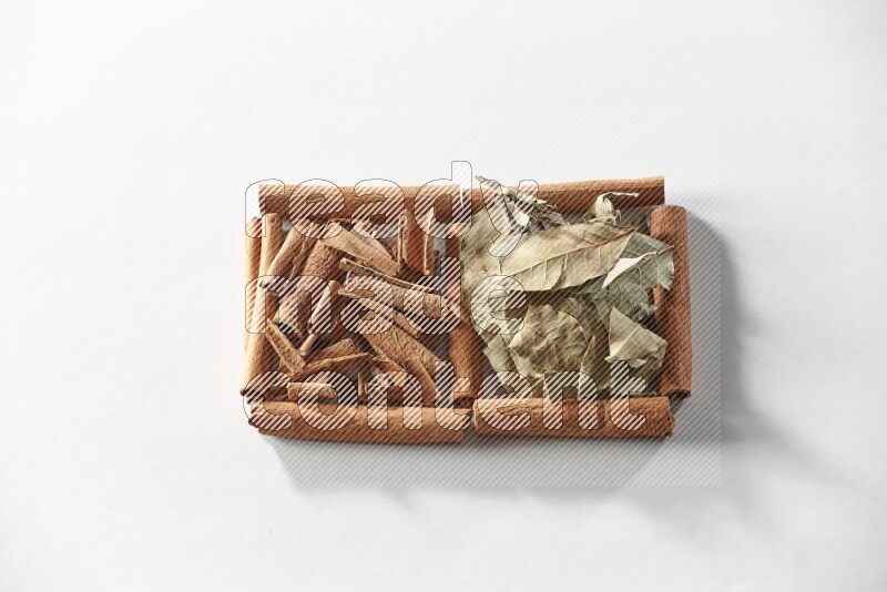 مربعان من أعواد القرفة ممتلئان بقطع من القرفة وأوراق الغار علي خلفية بيضاء