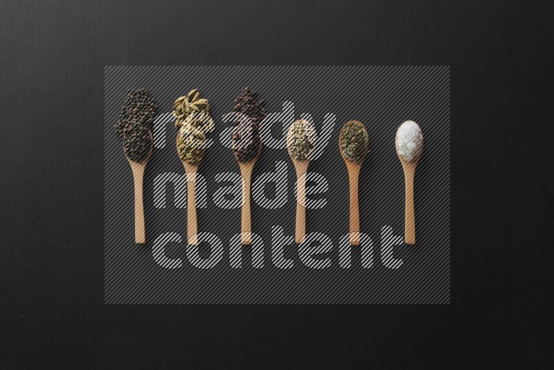 الفلفل الأبيض والقرنفل والهيل والملح والفلفل الأسود وريحان مجفف في معالق خشبية علي خلفية سوداء