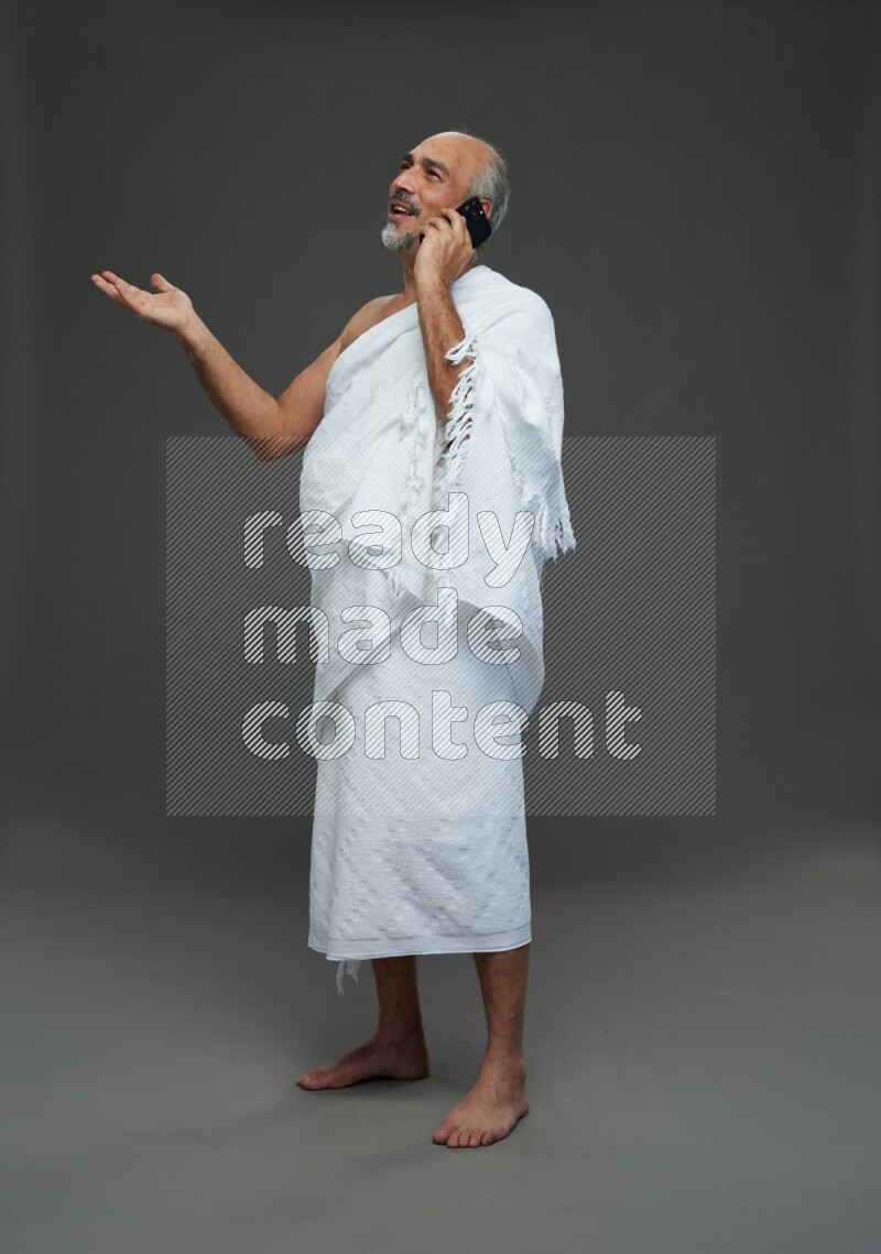 A man wearing Ehram Standing talking on phone on gray background