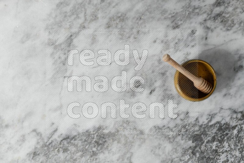 وعاء فخاري متعدد الألوان مع ملعقة عسل خشبية بداخله على خلفية من الرخام الرمادي