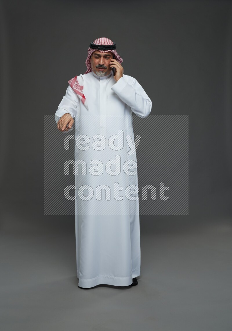 Saudi man with shomag Standing talking on phone on gray background