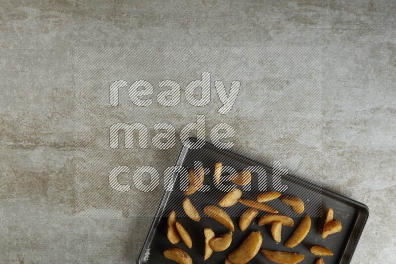 wedges potato in a black stainless steel rectangle tray on grey textured counter top