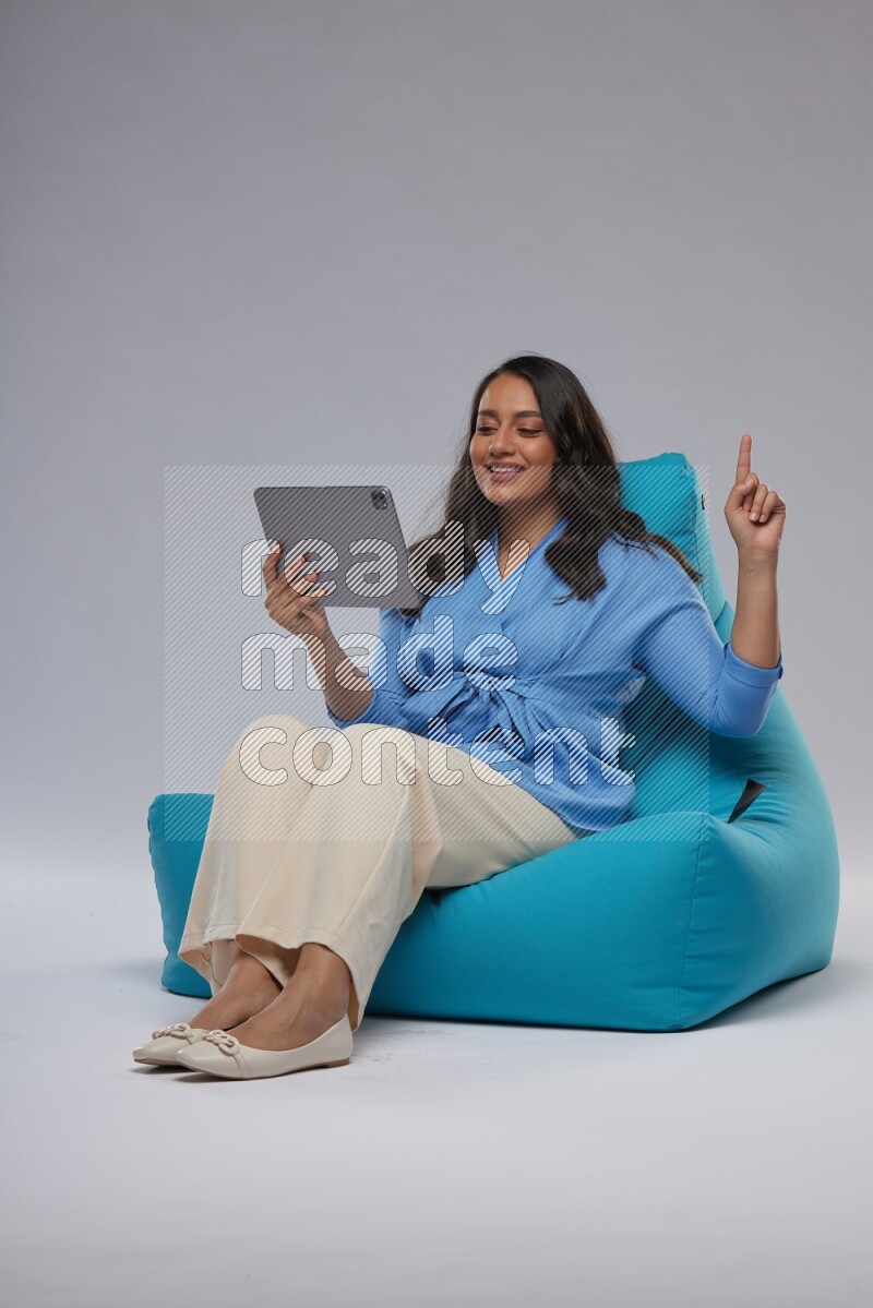 A woman sitting on a blue beanbag and working on tablet
