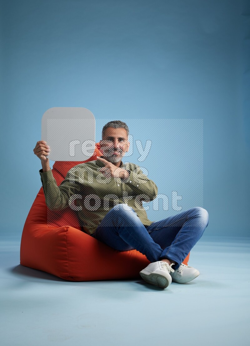 A man sitting on a orange beanbag and holding social media sign