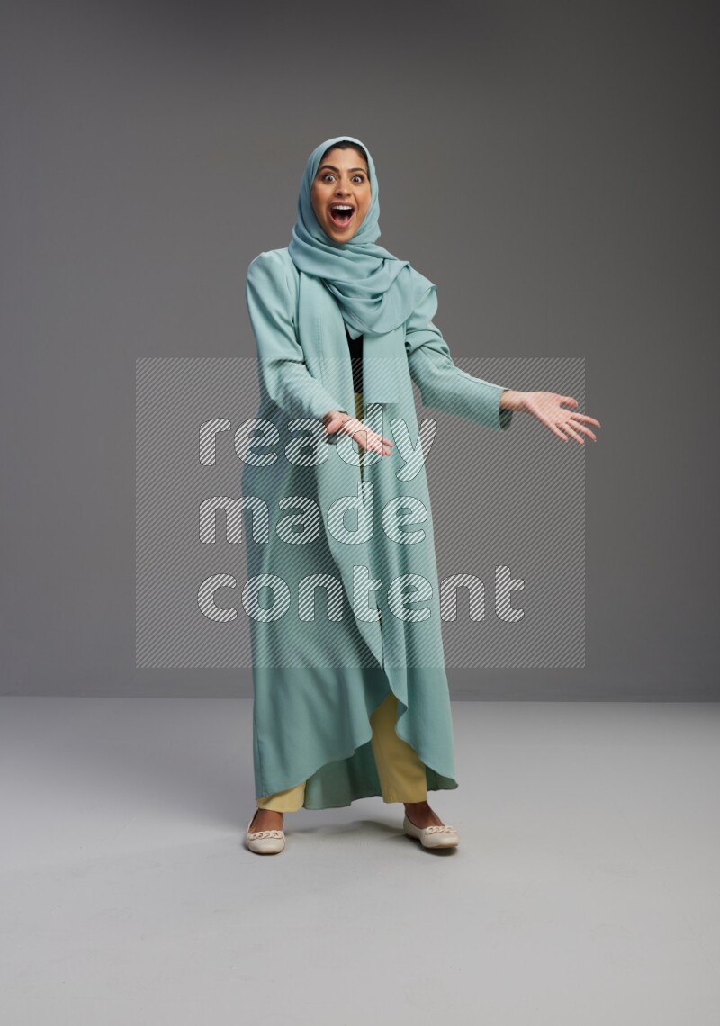 Saudi Woman wearing Abaya standing interacting with the camera on Gray background