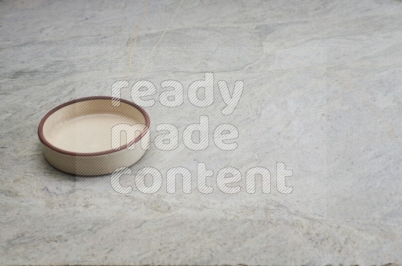 A beige pottery oven bowl on grey marble background