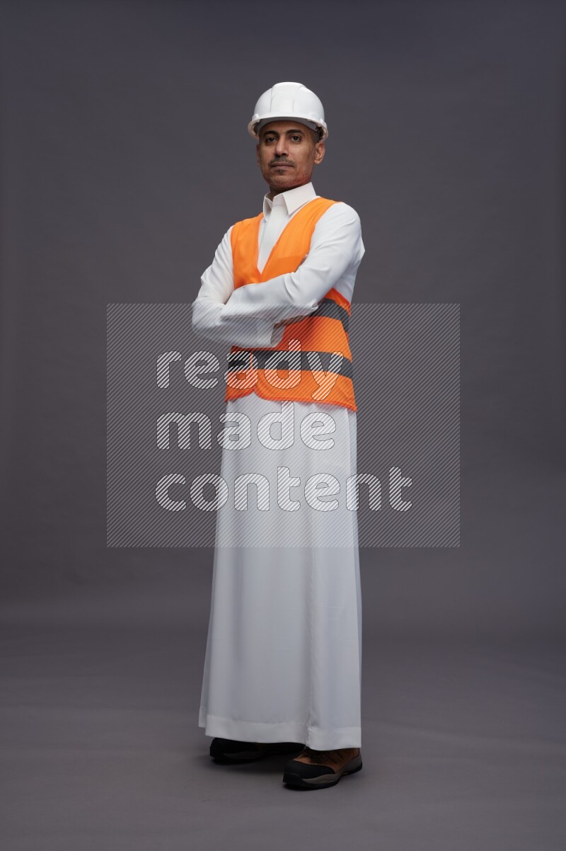 Saudi man wearing thob with engineer vest standing with crossed arms on gray background