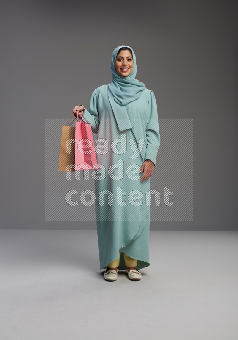 Saudi Woman wearing Abaya standing holding shopping bag on Gray background