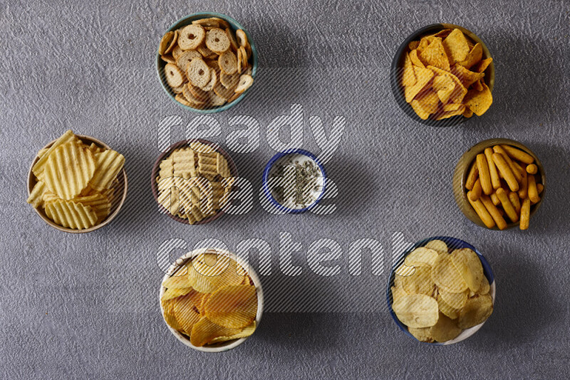 Assorted snacks in pottery bowls on grey background