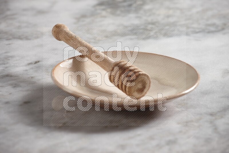 Beige pottery plate with wooden honey dipper in it on grey marble background