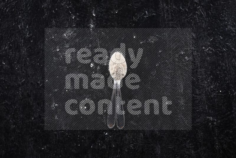 Two metal spoons full of onion powder on black background