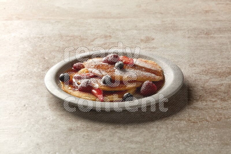 Three stacked mixed berries pancakes in a grey plate on beige background