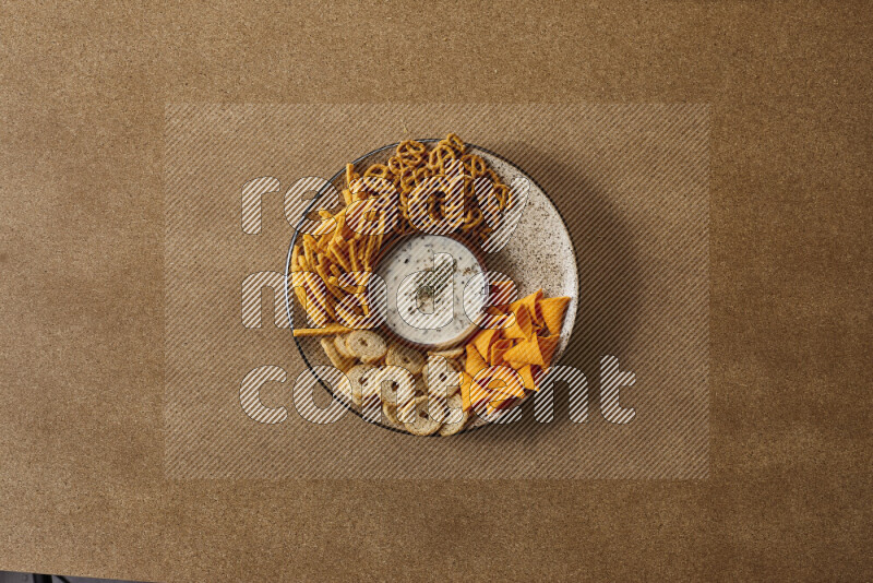 Assorted snacks on a pottery plate with a dipping on brown background