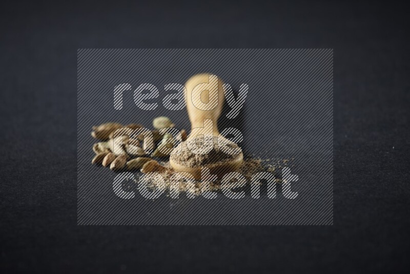 ملعقة خشبية ممتلئة ببودرة الهيل وحبوب الهيل بجانبها على خلفية سوداء