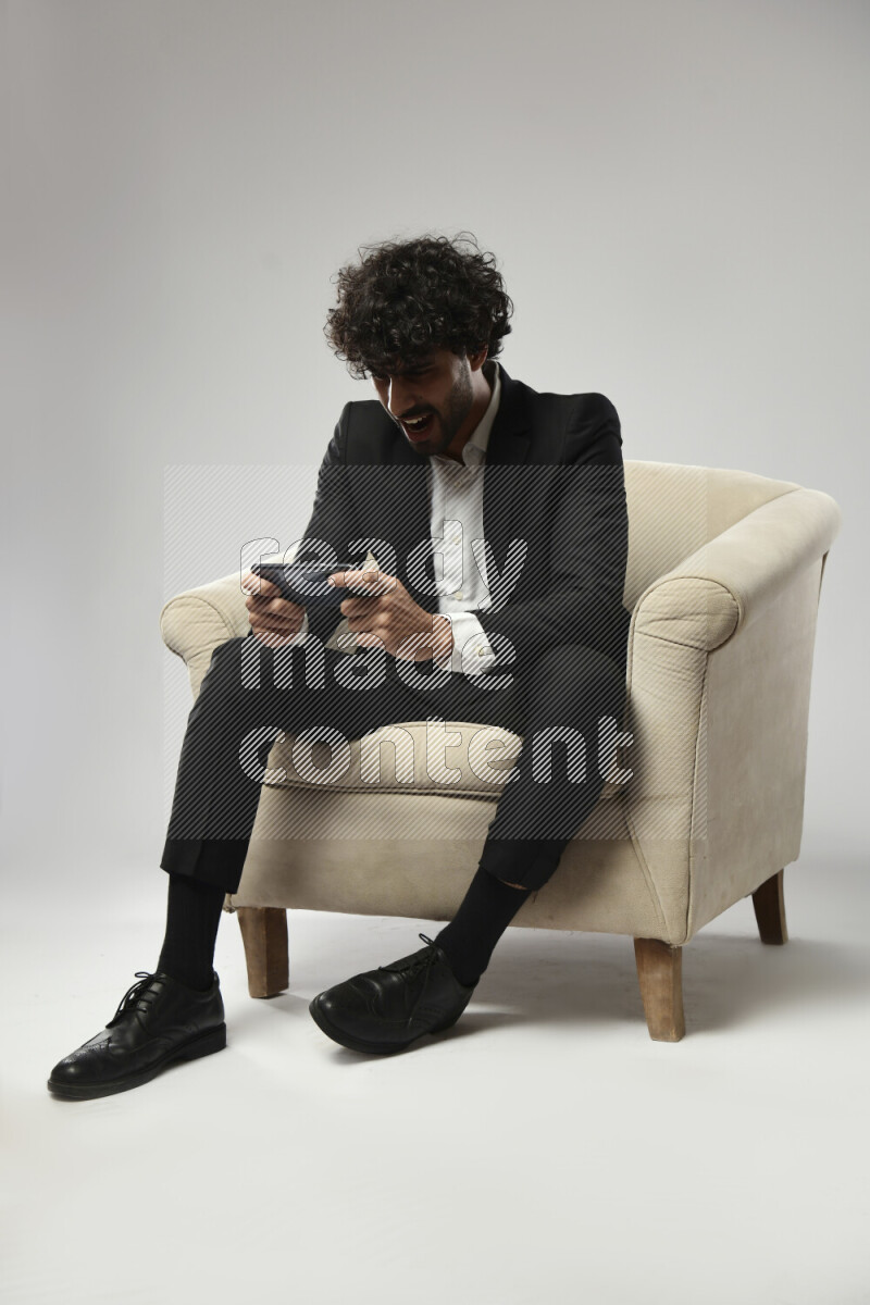 A man wearing formal sitting on a chair gaming on the phone on white background