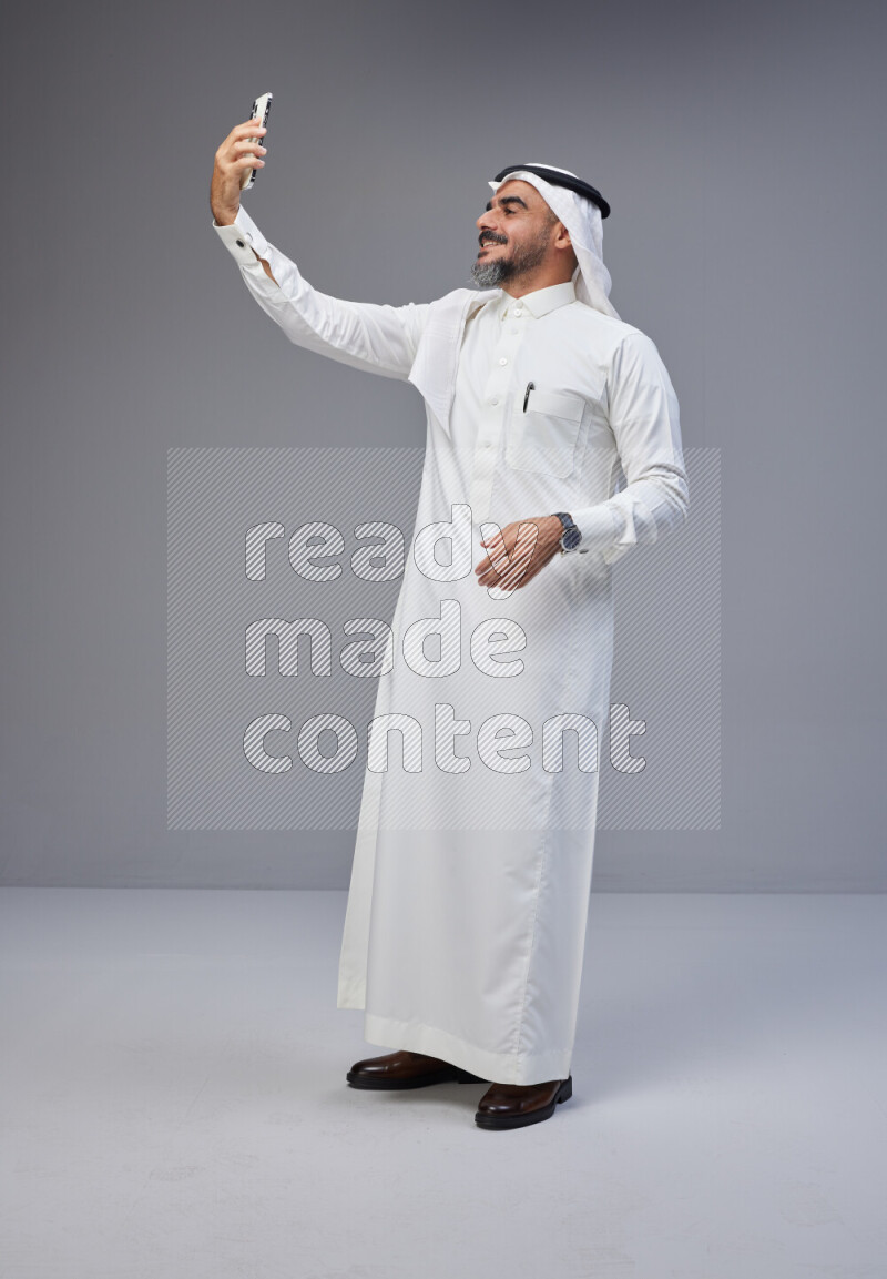 رجل سعودي يرتدي ثوب وشماغ ابيض يلتقط سلفي بجواله