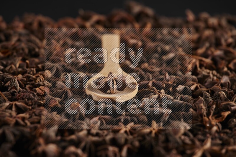 Star Anise in a wooden spoon on more stars anise filling the frame on black flooring