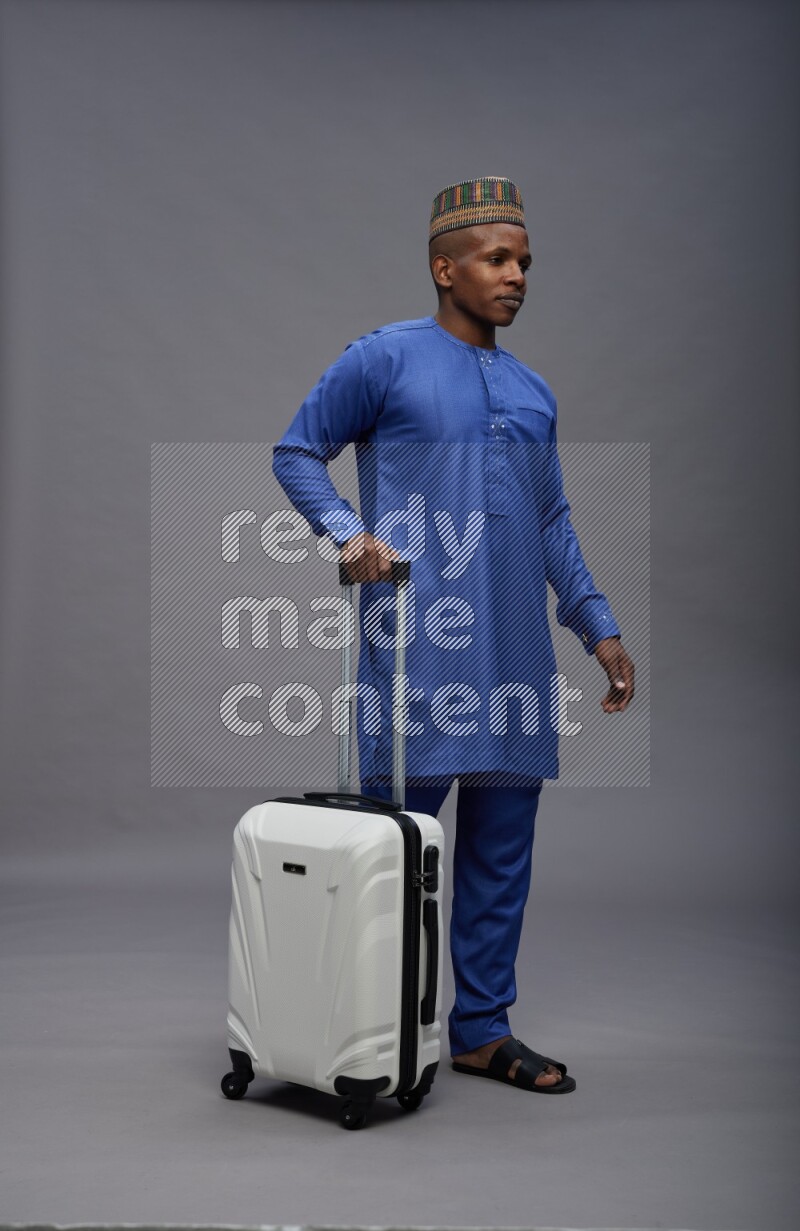 Man wearing Nigerian outfit standing holding bag on gray background