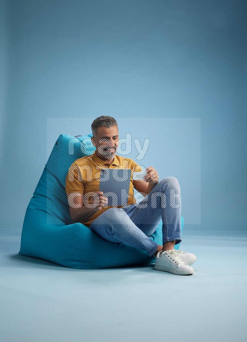 A man sitting on a blue beanbag and holding ATM card with tablet