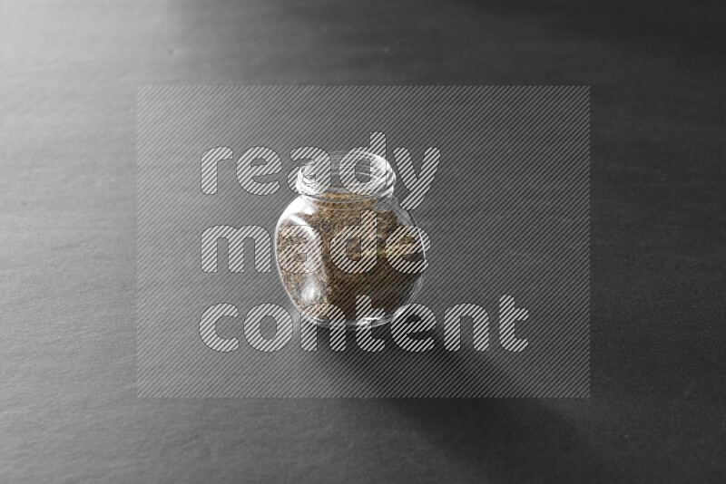 A glass spice jar full of cumin on black flooring